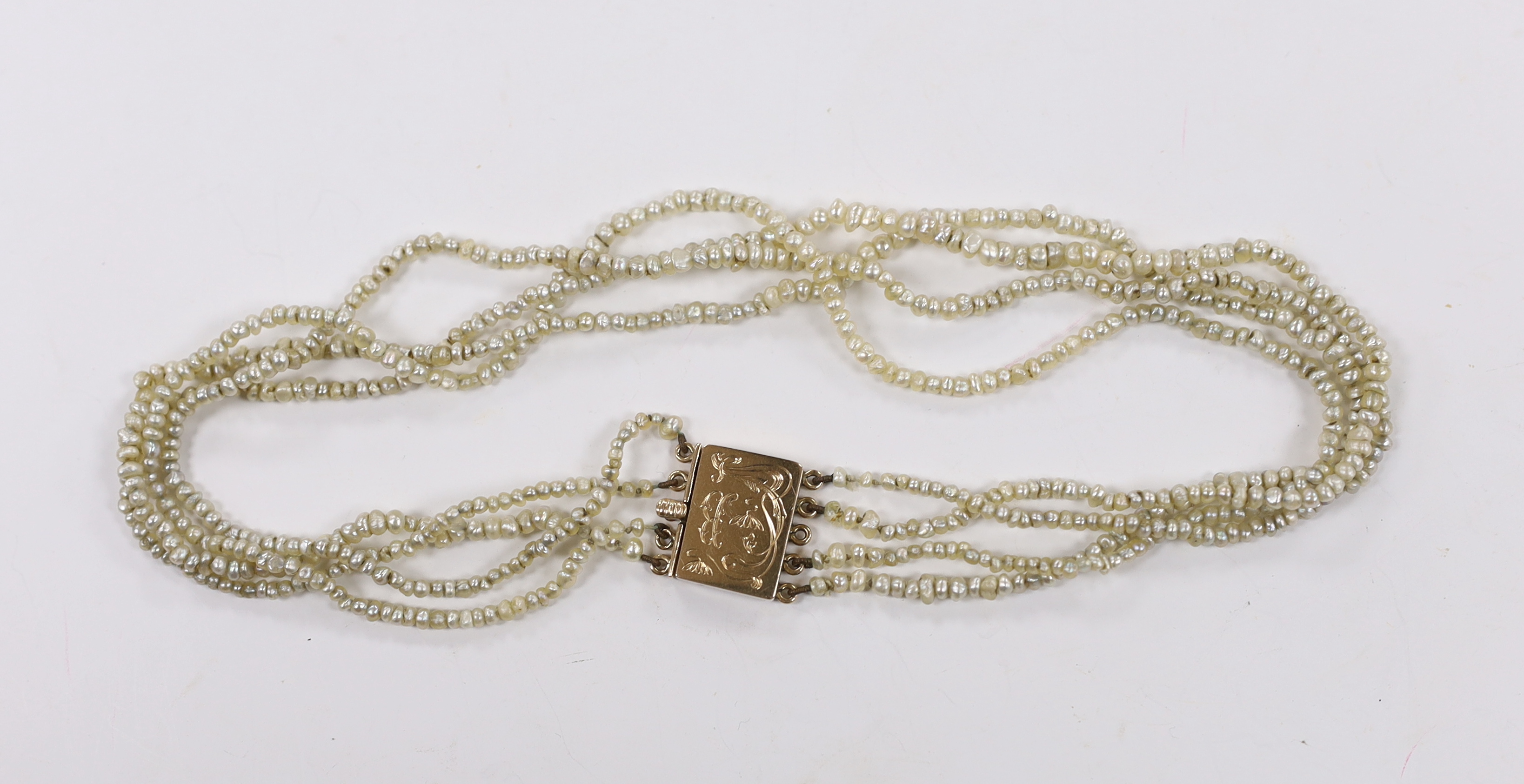 A Regency four (ex five) strand seed pearl choker necklace, with rectangular engraved yellow metal clasp, 37cm.